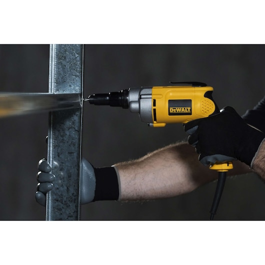 A person wearing gloves uses a yellow and black DEWALT DW268 electric screwdriver to drill into a metal frame.
