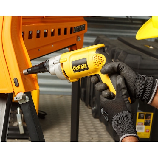 Gloved hands use a DEWALT DW269 electric screwdriver to fasten a metal frame in a workshop setting.