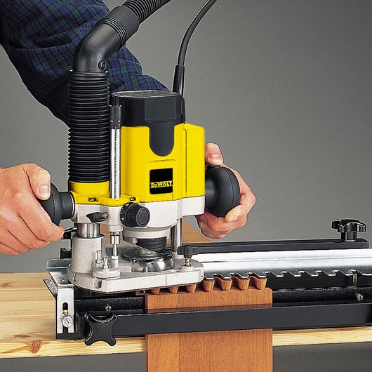 Person using a DEWALT DW622K router to cut wood with precision guide.