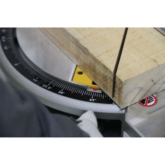 Close-up of a miter saw cutting wood at a 45-degree angle, showing the scale and gloved hand adjusting the tool.