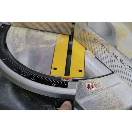 Close-up of DEWALT DW714 mitre saw with wood, angle gauge, sawdust, and safety warning visible.