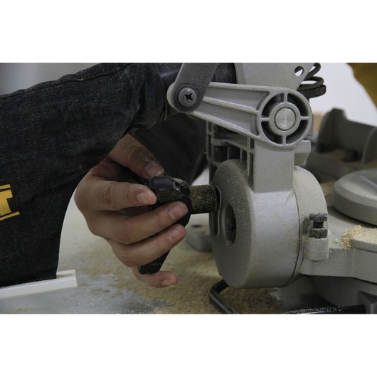 Hand adjusts the DW714 DEWALT miter saw, surrounded by sawdust during woodworking.
