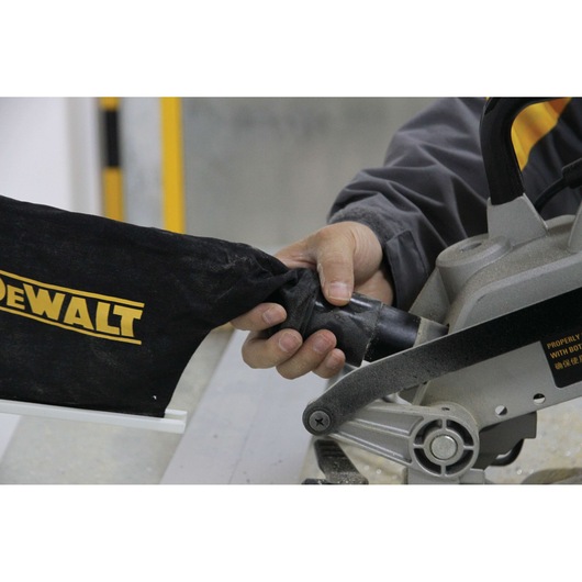 Hand attaching dust bag to a DEWALT miter saw, close-up of tool and bag connection.