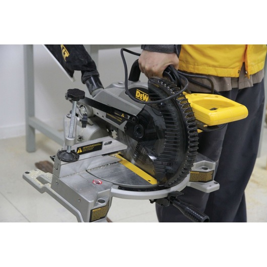 Person holding DEWALT DW714 miter saw, used for precise wood cutting in workshop.