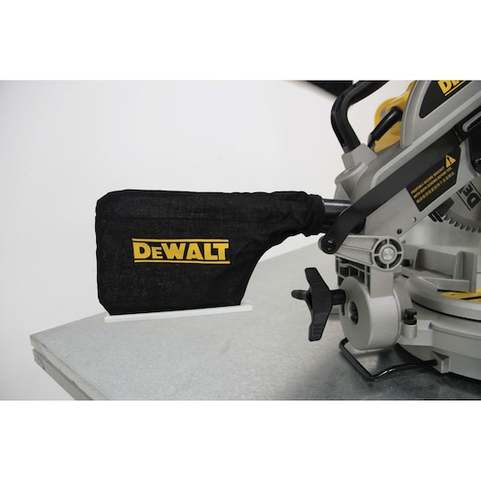 Close-up of a DEWALT miter saw with a black dust bag attached, placed on a metal surface.