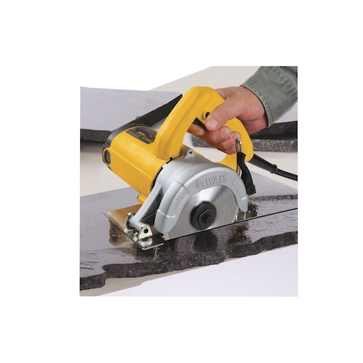 A close-up of a DEWALT DW862 handheld electric tile cutter being used to cut a piece of stone or tile. The tool is yellow and silver, and a person's hand is holding the handle while making a straight cut.