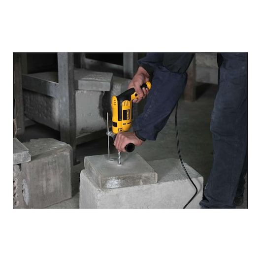 A person is using a yellow DEWALT electric drill to drill a hole into a concrete block in an industrial setting.