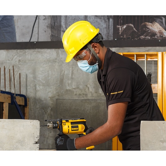 Worker uses DEWALT drill, models DWD024-QS and DWD024, for concrete drilling in construction setting.
