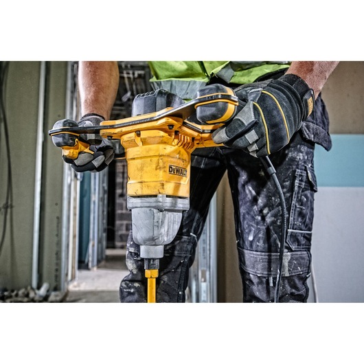 Person operating a DEWALT DWD241 mixer drill on a construction site, wearing gloves and workwear.