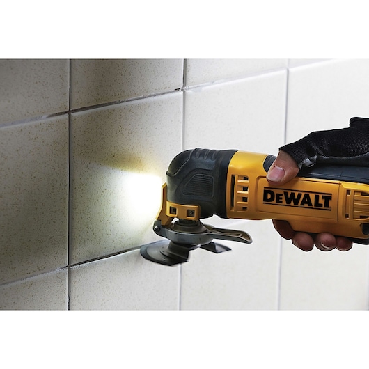 DEWALT oscillating multi-tool cutting tile grout with attached light, held by gloved hand.