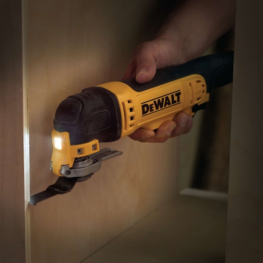 DEWALT oscillating multi-tool cutting wood, held by hand during precise work inside a cabinet.