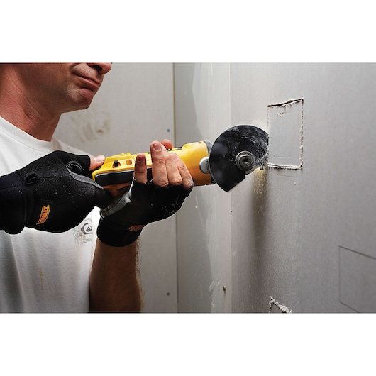 Person using a DEWALT oscillating tool to cut a square in a drywall panel, wearing gloves for safety.