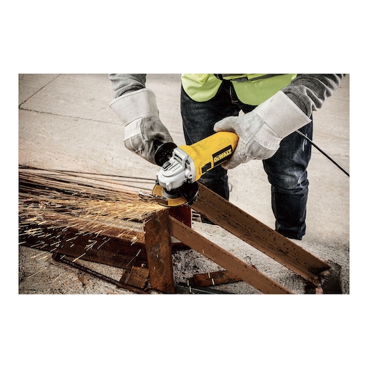 A person wearing safety gloves uses a DEWALT DWE4010 angle grinder to cut a metal beam, with sparks flying from the grinding area.