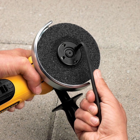 Hands adjust a DEWALT angle grinder wheel with a wrench on a concrete surface.