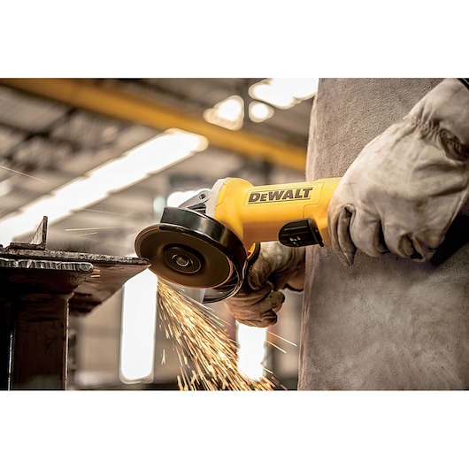 A person wearing protective gloves operates a DEWALT angle grinder, producing sparks while grinding a metal surface in an industrial setting.
