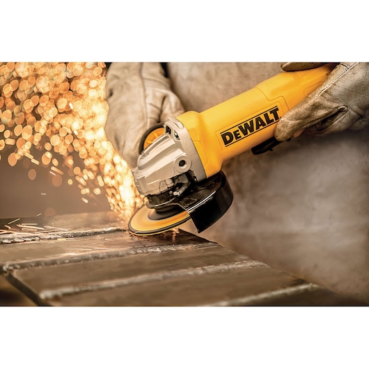 A person wearing protective gloves is using a yellow DEWALT angle grinder to cut or grind metal, with sparks flying from the surface.