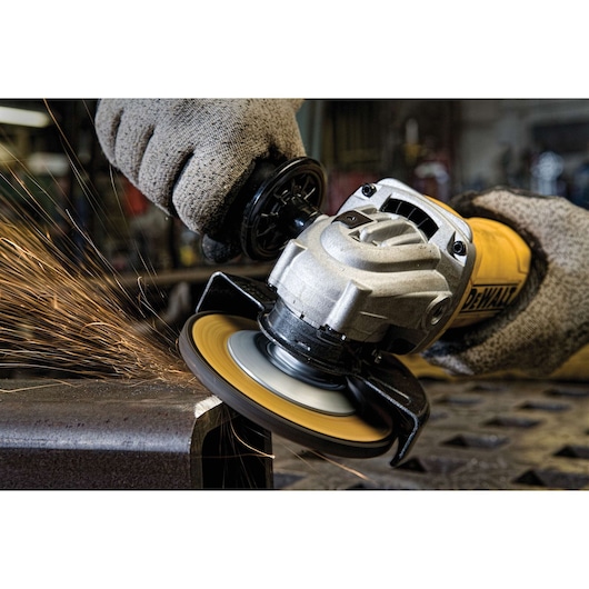 A close-up of a person using a DEWALT angle grinder to grind a piece of metal, with sparks flying. The person is wearing protective gloves.
