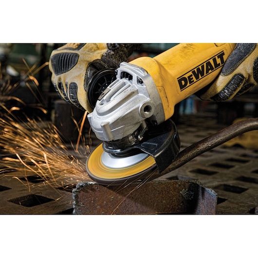 A close-up of a DEWALT angle grinder in use, producing sparks as it grinds a piece of metal. The tool is operated by a person wearing protective gloves.