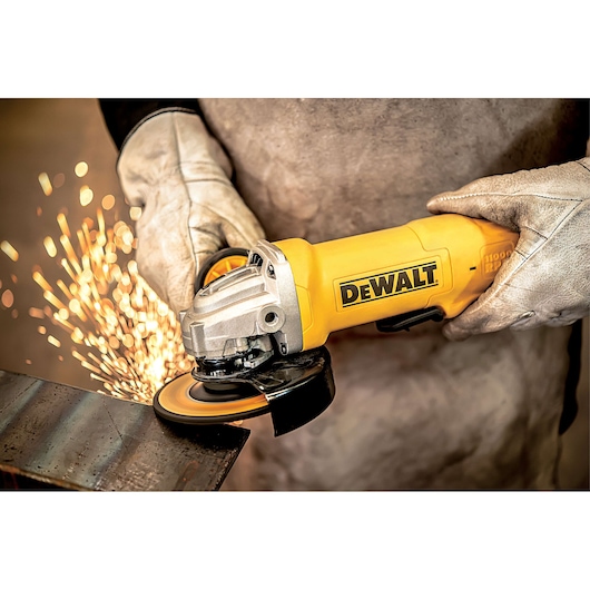 A person wearing protective gloves is using a yellow DEWALT angle grinder to cut or grind a piece of metal, with sparks flying from the contact point.