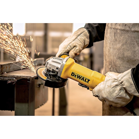 A person wearing protective gloves uses a yellow DEWALT angle grinder to cut a piece of metal, creating sparks.