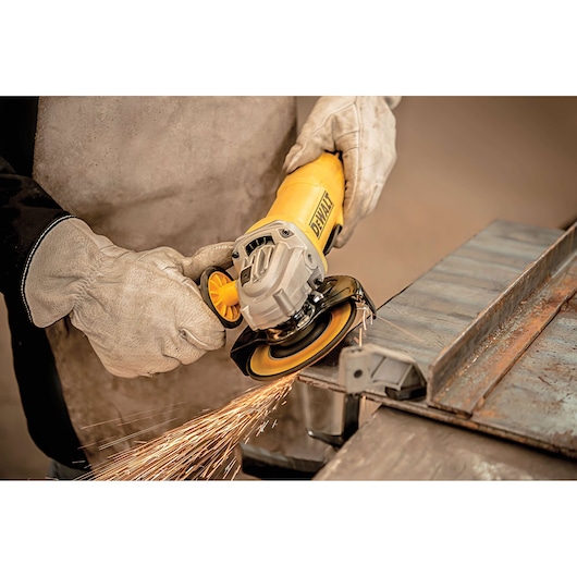 A person wearing protective gloves uses a yellow DEWALT angle grinder to cut a piece of metal, producing sparks.