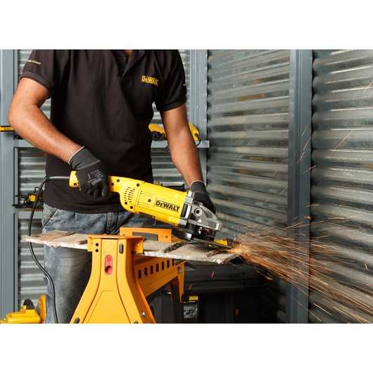 Person using a DEWALT DWE493 angle grinder on metal, producing sparks in a workshop setting.