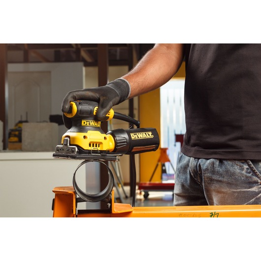 Person using a DEWALT DWE6411 sander on a metal pipe in a workshop setting.