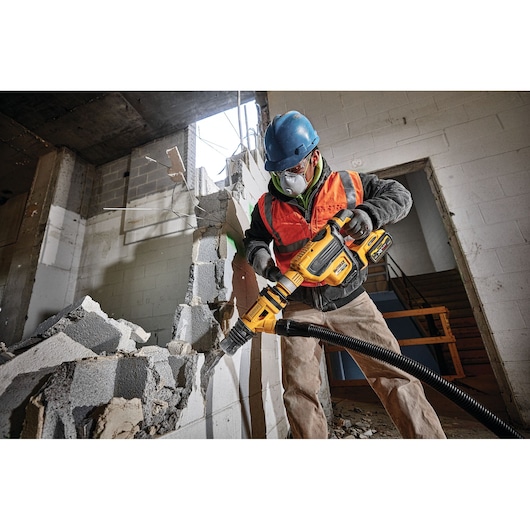 Person using a DEWALT demolition tool to break a concrete wall in a construction site. Protective gear worn.