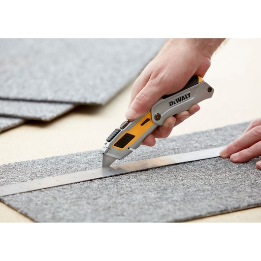 DEWALT utility knife cutting carpet along a metal ruler.