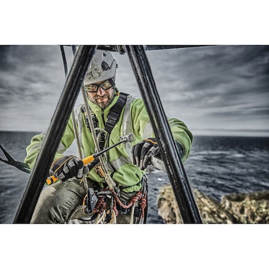 Worker with safety harness using a DEWALT tool on a structure outdoors near the sea.