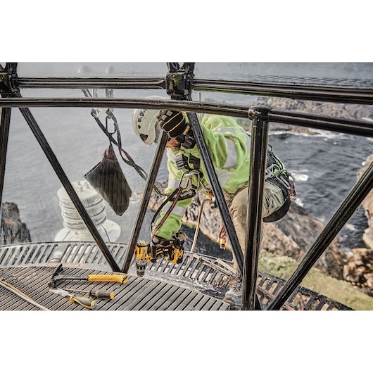 Worker using DEWALT tools inside a lighthouse with a sea view, wearing safety gear and helmet.