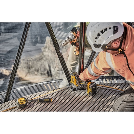 Worker uses DEWALT tools and drill while wearing safety gear at construction site with metal flooring.