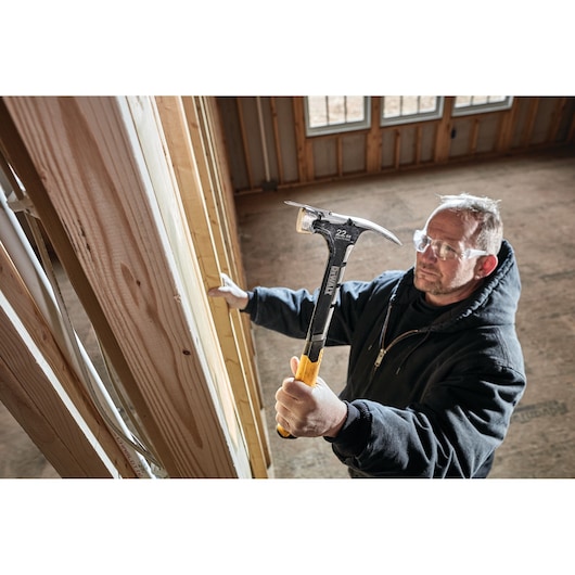 Person holding a DEWALT hammer, working on wooden framing inside a construction site.