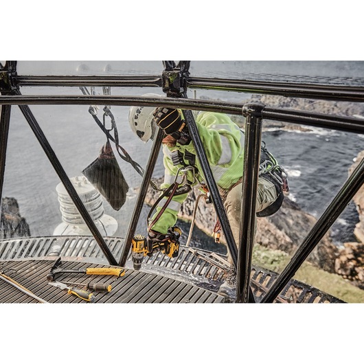 Worker in safety gear using DEWALT tools on metal structure overlooking the sea.