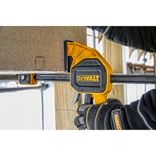 DEWALT clamp holding wood in place, used by a person wearing gloves during a construction project.