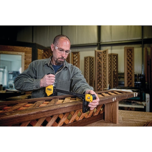 Person uses a DEWALT clamp to secure a wooden frame in a workshop. Face is blurred for privacy.