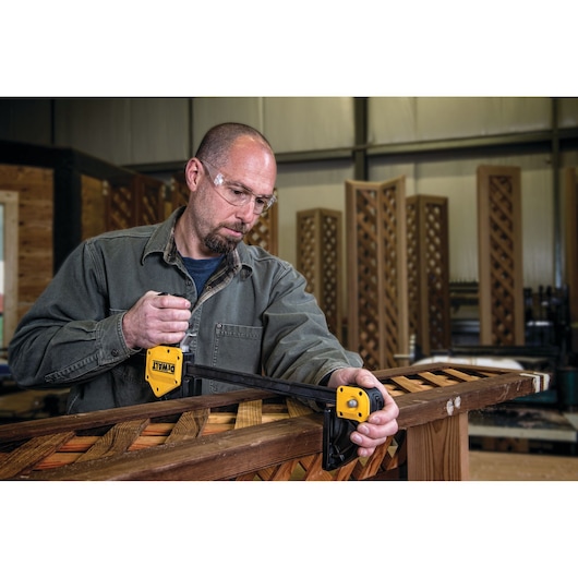 Person using a DEWALT bar clamp to secure wooden boards in a workshop.