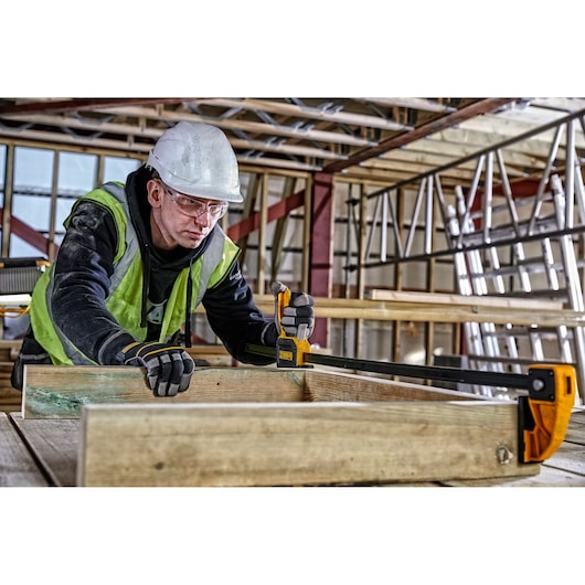 Person using DEWALT bar clamp DWHT0-83187 to secure wooden boards at a construction site.