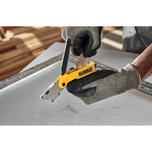 Gloved hands change blade on yellow DEWALT utility knife above a ruler and work surface.