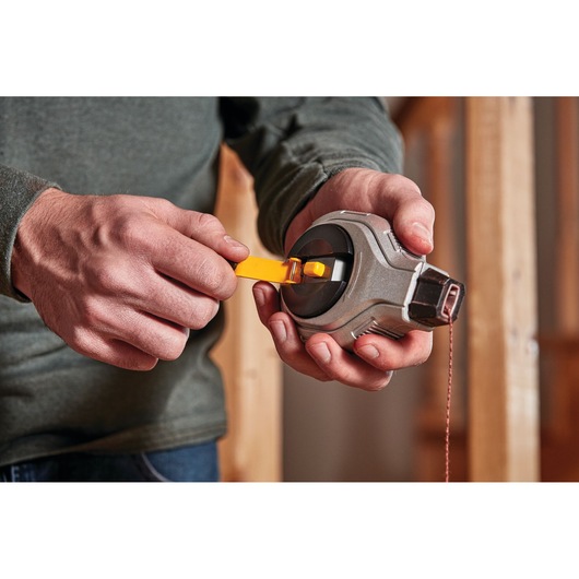 Person holding and winding a DEWALT chalk line tool with a yellow handle in a construction setting.