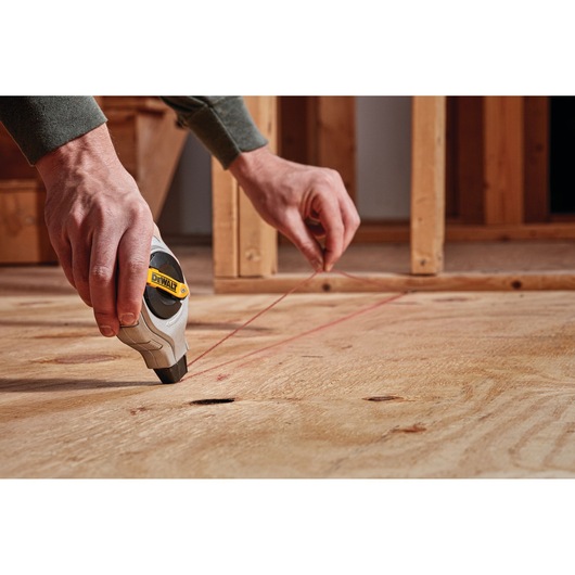 Person uses DEWALT chalk line tool on plywood floor at construction site.