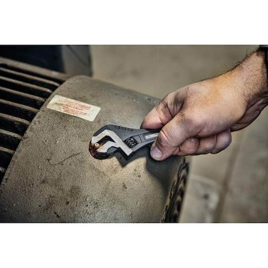 Hand uses DEWALT adjustable wrench to turn a bolt on industrial equipment.