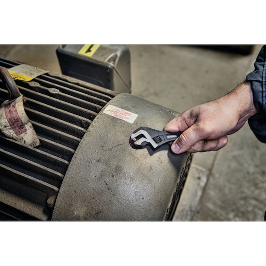 Hand using a DEWALT adjustable wrench to tighten a bolt on industrial equipment.