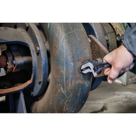 Hand using a DEWALT adjustable wrench to tighten a bolt on a large, industrial metal pipe.