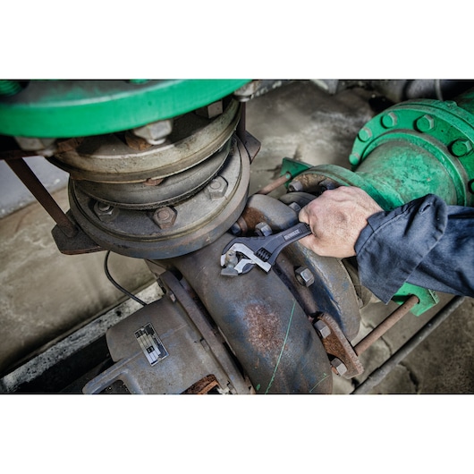 Hand uses DEWALT adjustable wrench on an industrial pipe joint with green fittings.