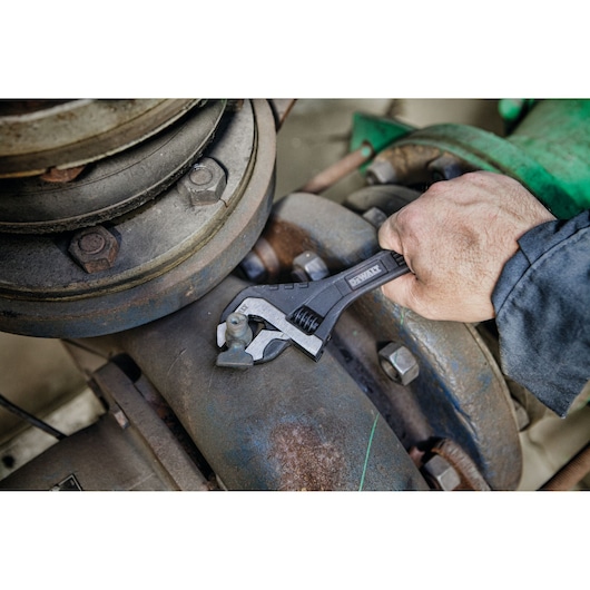 Hand uses DEWALT adjustable wrench on industrial pipe bolt.