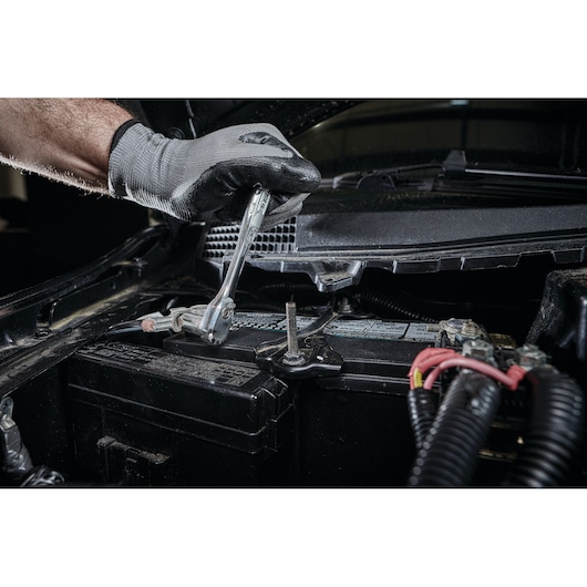 Gloved hand uses a DEWALT ratchet wrench to work on a car battery under the hood.