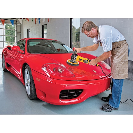 A person is polishing the hood of a red sports car with a DEWALT DWP849X polisher in a garage.