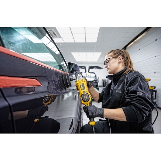 Person polishing a car door using a yellow DEWALT DWP849X tool in a workshop.
