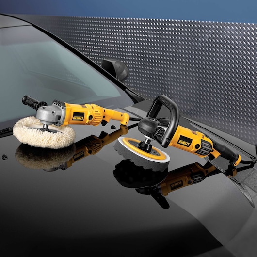 Two DEWALT polishing tools are placed on the hood of a black car, each with a different polishing pad attached. The yellow and black tools are used for auto detailing and surface polishing.
